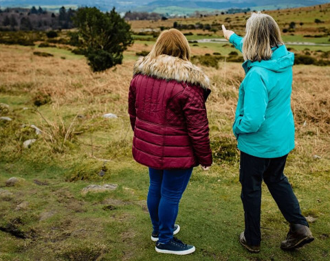 Two women are standing on Dartmoor. One of the women is pointing into the distance.