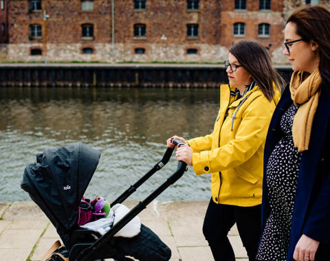 Two women are walking together at Exeter Quay. One woman is pregnant and the other is a new parent pushing a pram.